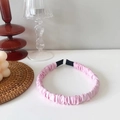 Detalle de diadema rosa fruncida de satén con puntas negras sobre superficie blanca - Rosa Claro