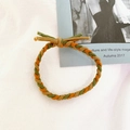 Detail view of a braided elastic hair tie featuring green, brown, and orange interwoven cords - Orange Green