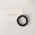 Detailed view of a black spiral hair tie on a minimalist beige background with a card - Black