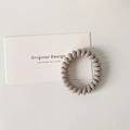 Detailed view of neutral grey spiral hair tie on minimalist white display card background - Light Gray