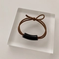 Gros plan d'un élastique à cheveux marron avec un tube incurvé noir poli sur bloc - Corde à Cheveux Tube Rond Noir