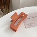 Close-up of a coral orange matte rectangle hair claw clip on a stylish white desk - Orange