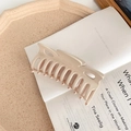Detail view of large matte beige shark hair claw clip on an open book for styling - Beige