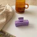 Detail of matte purple rectangular hair claw clip with cutout design on beige fabric - Purple