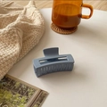 Macro shot of matte blue claw clip on a white table with a warm lifestyle background - 8cm / Blue Gray