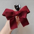 Detail of burgundy bow hair claw with pearl accents showing texture and hand-held scale - Burgundy