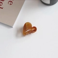 Detail view of a translucent amber heart-shaped hair claw clip on a minimalist white surface - Heart Shape (Amber Brown)
