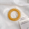 Vue détaillée d'un élastique spirale ambre mat posé sur un tissu de lin blanc minimaliste - Orange