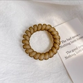 Dettaglio dell'elastico per capelli a spirale marrone opaco su carta decorata - Cachi
