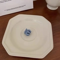 Detailed view of a small matte blue hair claw clip placed on a white ceramic plate - Fog Blue