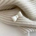 Detail of cream velvet bow hair clip styled on a matching knitted sweater surface - White