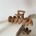 Detail view of large brown matte hair claw clip with wave design and metal spring - Tan