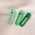 Macro detail of three matte green gradient oval hair clips on soft tulle fabric background - Green