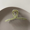 Macro detail of avocado green acrylic claw clip with cross twisted design on grey plate - Matcha Green