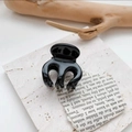Detailed view of mini glossy black hair claw clip with interlocking teeth on stone surface - Solid Black