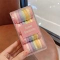 Détail d'un ensemble d'élastiques à cheveux macaron colorés dans une boîte transparente - Série Macaron