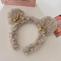 Dettaglio di fascia di peluche grigia con orecchie da orso, campanelli dorati e fiocchi - Beige