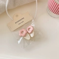 Dettaglio di fermagli per capelli a fiori rosa in confezione su maglia e perle - Bianco Latte