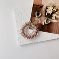 Detail view of brown spiral hair tie and silver U-shaped earrings on textured stone - Brown