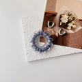 Close-up of a blue spiral hair tie and silver U-shaped metal earrings on a white stone - Blue