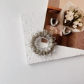 Close-up of grey spiral hair tie and silver heart earrings on a white textured stone base - Gray