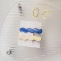 Dettaglio di fermagli per capelli ondulati in acetato e orecchini ovali dorati eleganti - Stile a Onda Sottile