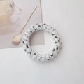 Spiral hair tie with black stars on transparent resin shown on a bright table - White Star