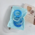 Detail view of blue gradient spiral hair ties in a clear pouch on a glass tray - Blue
