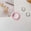 Flat lay of transparent pink spiral hair tie and silver C-shaped zircon earrings - Forest Pink