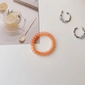 Macro shot of an orange spiral telephone cord hair tie on a decorative desk setup - Transparent Orange