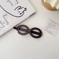 Detail view of the matte dark brown infinity shape hair clip on a minimalist white desk - Infinity Matte Dark Brown