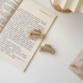 Détail de deux petites pinces à cheveux rectangulaires mates sur un livre ouvert - Carré Khaki