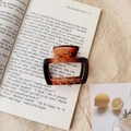 Close-up of amber square hair claw clip with shell texture on vintage book page - Glossy Rectangular (5003918933157) / Glossy Amber Dark Color