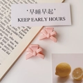 Detail view of two pink matte bow hair clips on a decorative lifestyle background - Matte Light Pink (Plastic)