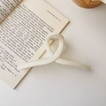 Detailed view of a 15cm cream-colored extra-large shark hair claw clip on an open book - Matte Cross Style / Extra Large / Matte White