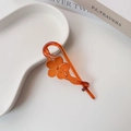 Detailed view of amber tortoise shell hair clip featuring hollow floral design on a ceramic plate - Glossy Flower Orange