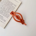 Matte orange twisted hair clip placed on a book showing a sleek braided design texture - Matte Orange