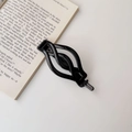 Close-up of a black hollow wave-shaped hair clip placed on an open vintage book - Glossy Black