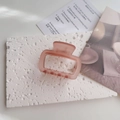 Close-up of matte dusty pink rectangular hair claw clip on white textured stone base - Brown