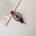 Detail of dark purple matte hair claw with twisted hollow design on an open book - Matte Purple