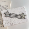 Dettaglio del pettine per capelli ondulato con stelle di strass su un libro aperto - Stella Bianco Argento