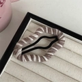 Detail of brown and white striped knit fabric hair clip on a beige jewelry cushion - Brown