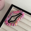 Macro view of a colorful handmade yarn-wrapped cloud hair clip on a beige velvet tray - Pink