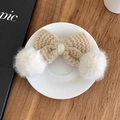 Dettaglio del fermaglio per capelli in maglia kaki con pompon bianchi su tavolo di legno - Cachi