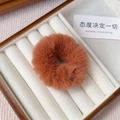 Close-up of caramel plush hair tie made of fluffy faux rabbit fur on wood jewelry box - Caramel color