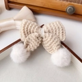 Dettaglio di un fermaglio per capelli a fiocco in maglia crema con pompon bianchi soffici - Cachi
