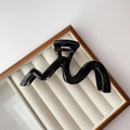 Close-up of black glossy wave hair claw clip on white velvet display tray with wood frame - Glossy Black
