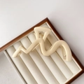 Macro detail of wave-shaped cream hair claw clip with silver spring on velvet jewelry tray - Glossy Off-White