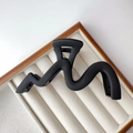 Detailed view of a large matte black wave hair claw clip on a white velvet display tray - Frosted / Matte Black