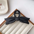 Close-up of matte black bow-shaped claw clip with wavy edges on white jewelry display box - Black